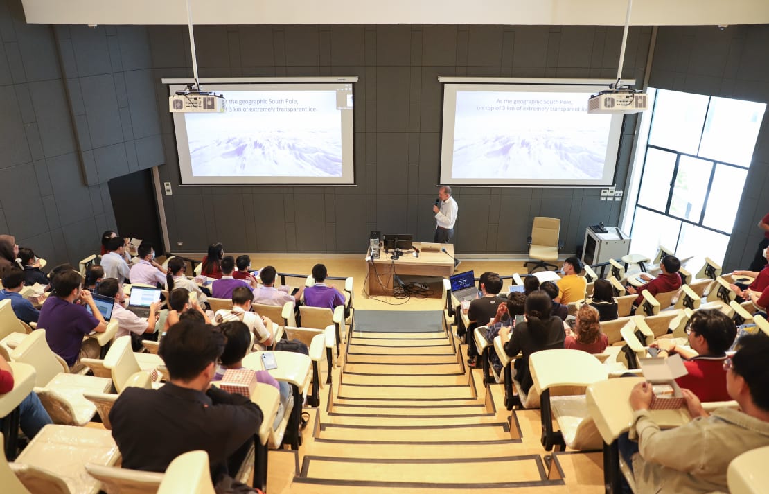 A man giving a public lecture in front of a crowded auditorium full of people