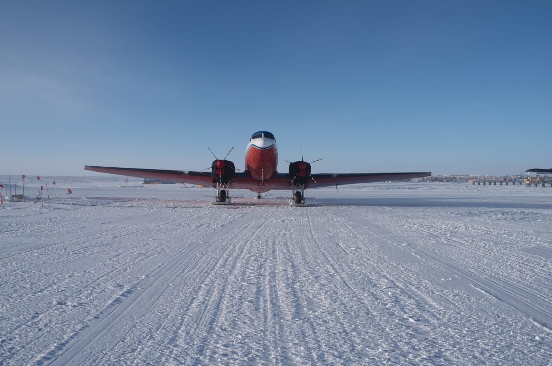 Front view of a Basler plane parked on the ice at the South Pole under blue skies.