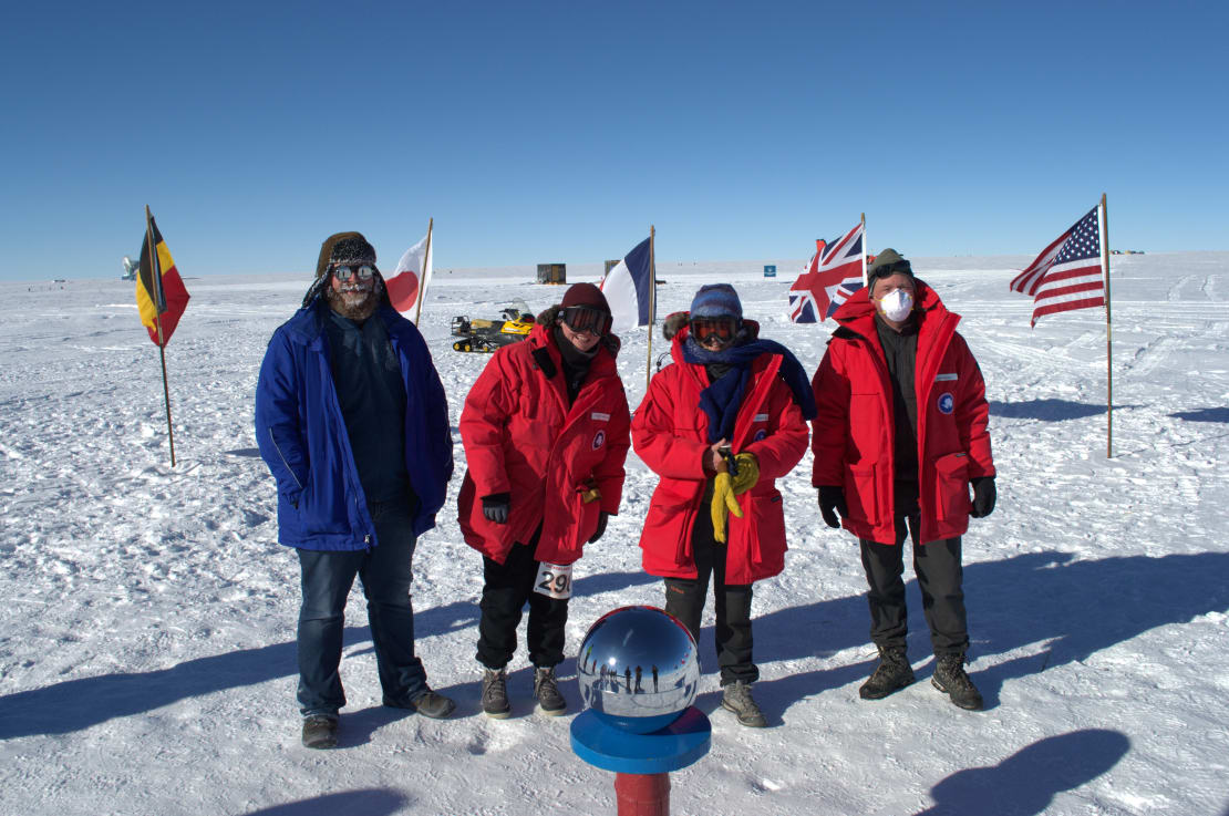 Four people posing in front of mirrored globe at ceremonial South Pole.