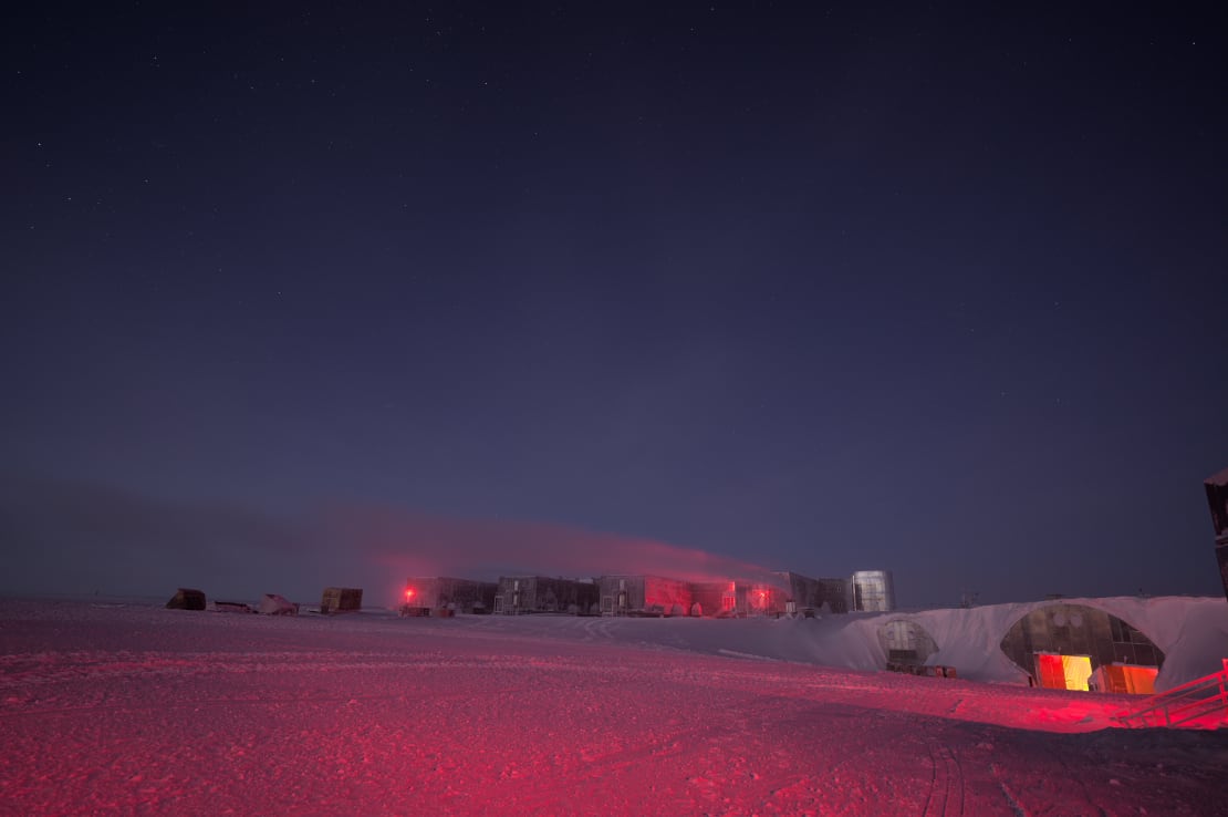 The South Pole station in the distance, with external red lights turned on.