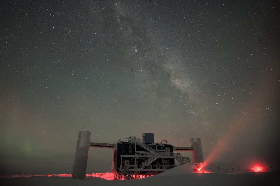 The IceCube Lab under the Milky Way with a few red lights on the surface nearby.
