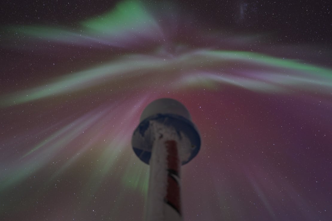 View up into aurora-filled sky from below ceremonial pole marker.