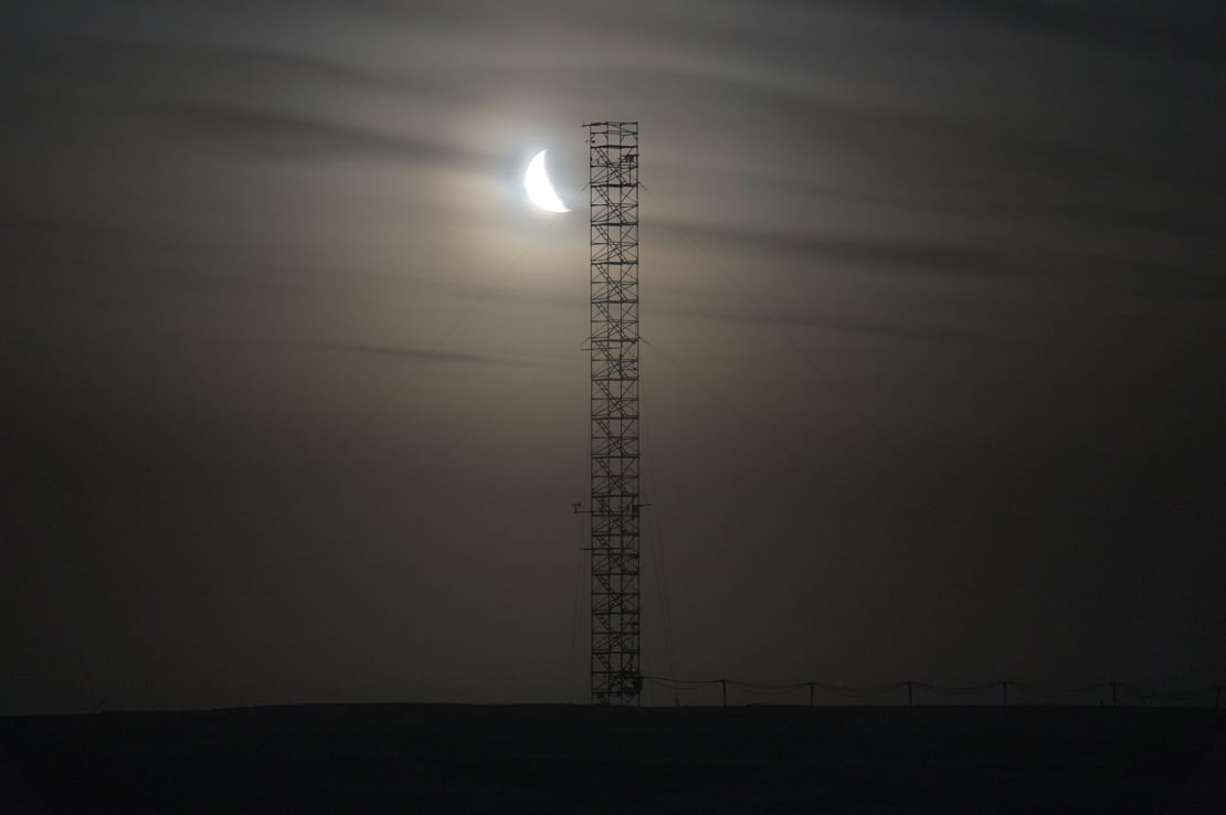 A bright moon shining through striated clouds in the dark sky, a silhouetted ARO tower in the foreground.