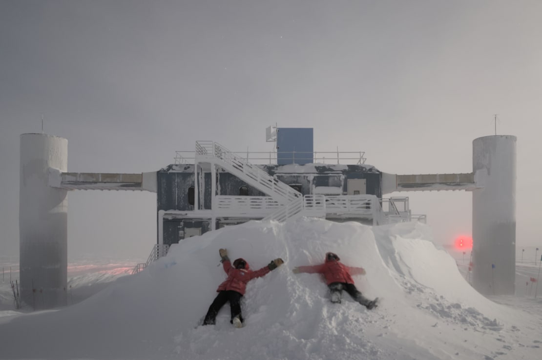 Two winterovers making snow angels in large snowdrift in front of the IceCube Lab.
