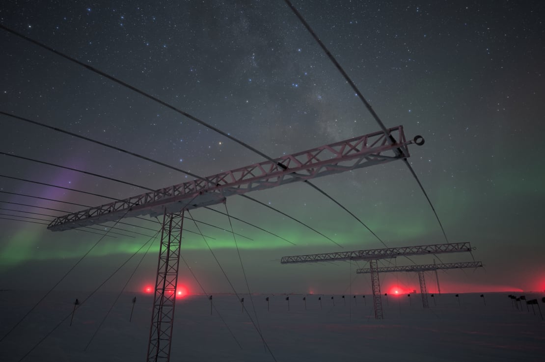 Winter skies and auroras seen through row of large antenna structures in the foreground.