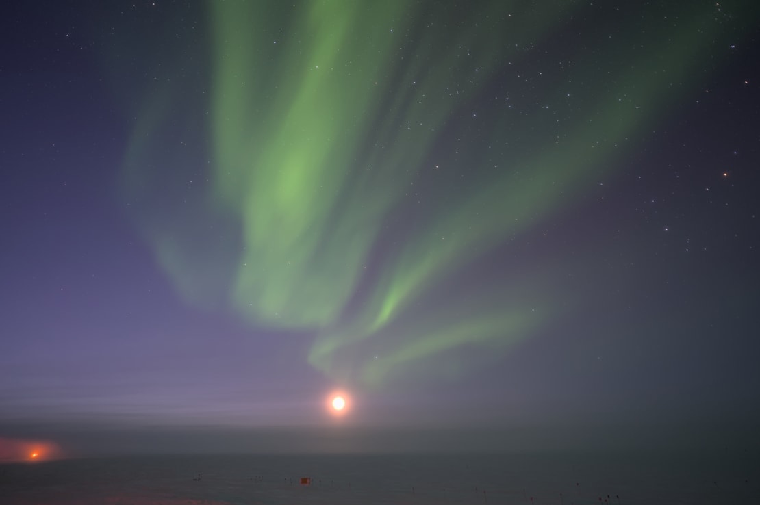 Swirling green auroras over a bright moon low in the sky.