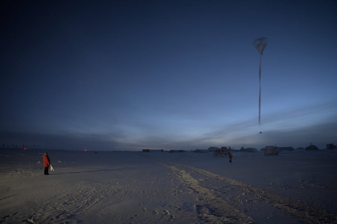 A person in red parka in distance off to the left with a weather balloon off to the right rising in the sky.