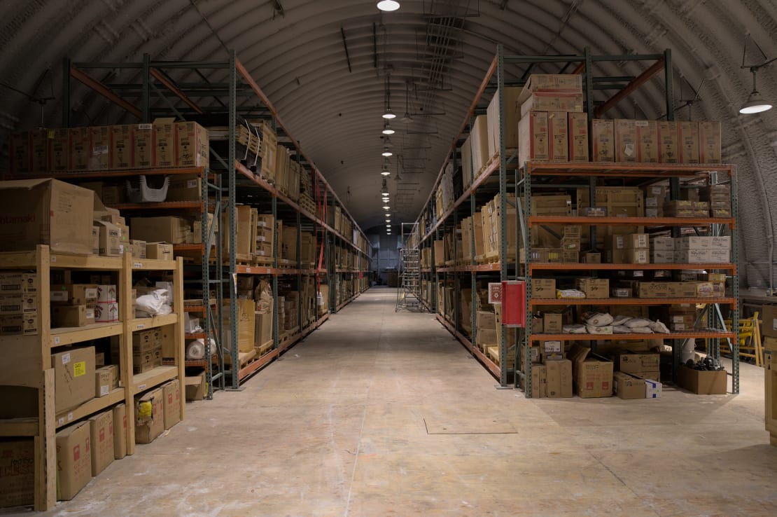 Long view of aisle in food storage warehouse, with tall shelves lined with boxes on both side.