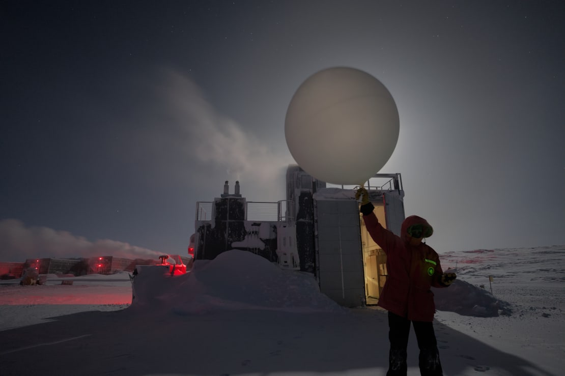 Large weather balloon being held overhead and blocking a bright moon just before launching.