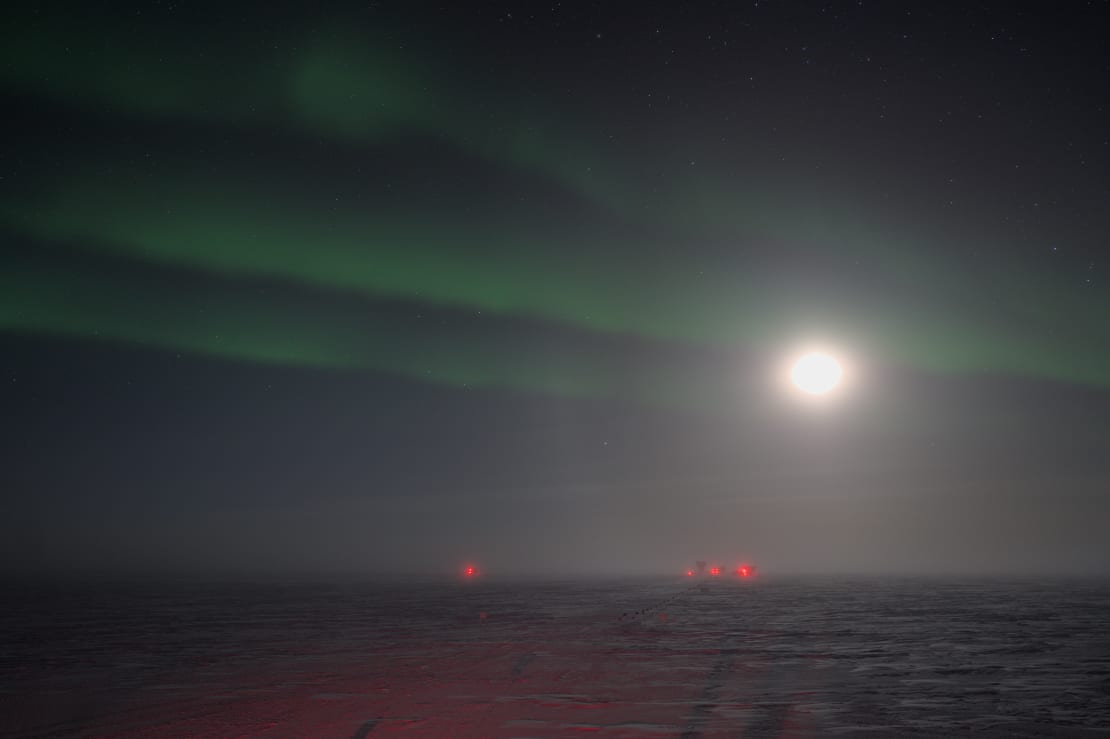 Green swaths of aurora across the South Pole winter sky lit by a bright moon.