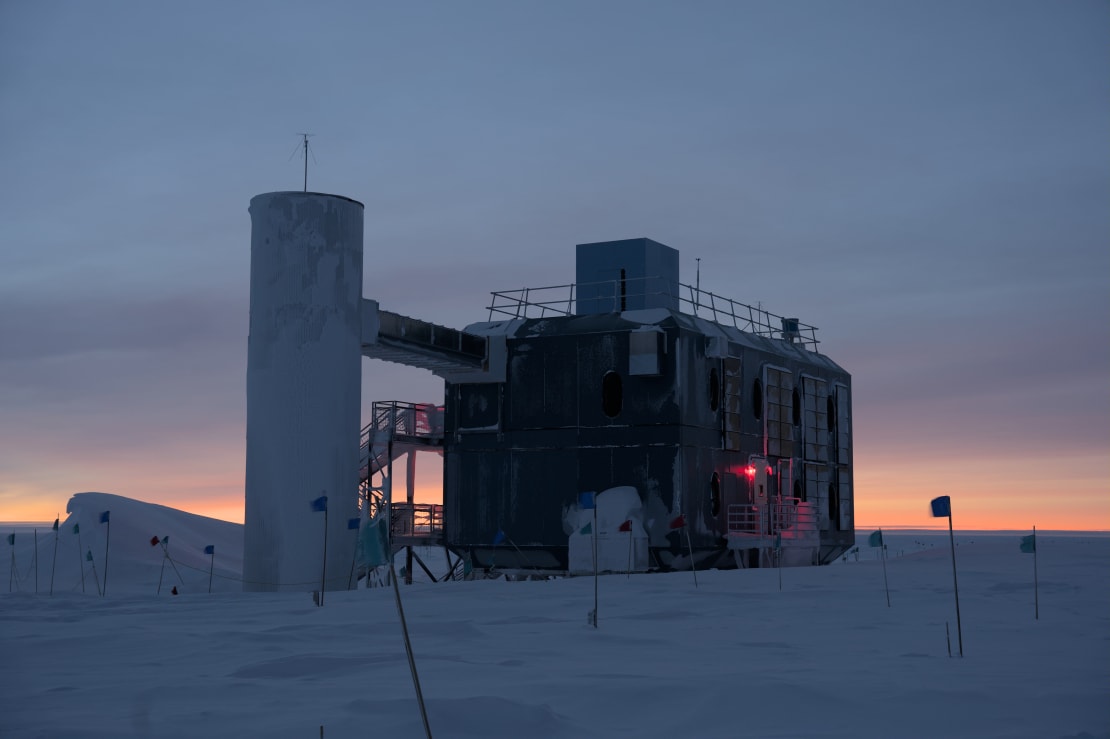 Orange light along the horizon before sunrise at the South Pole, IceCube Lab in foreground.