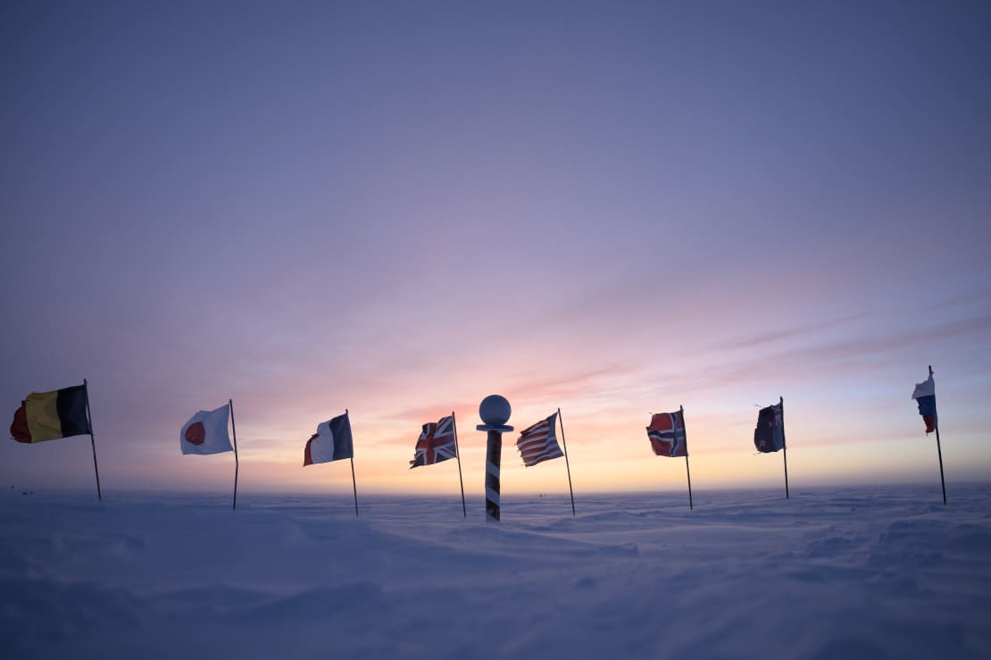 Brightening presunrise sky at the ceremonial Pole, with marker and flags still in shadow.