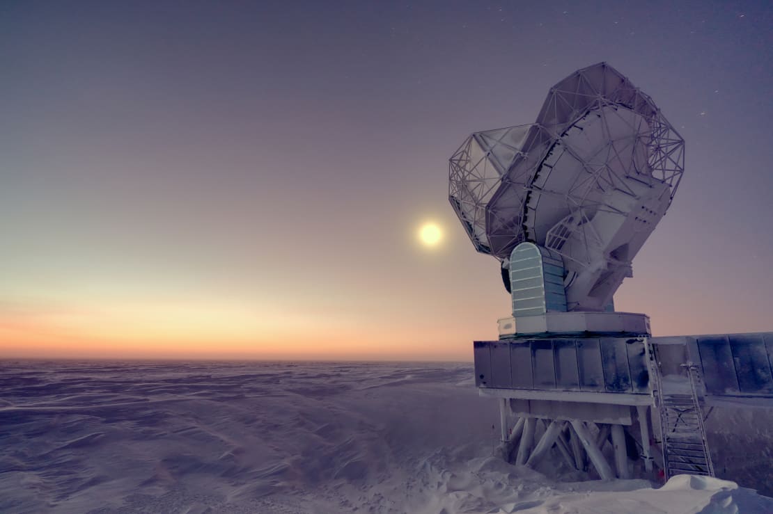 Bright moon behind the South Pole Telescope at twilight, soft orange light on horizon.