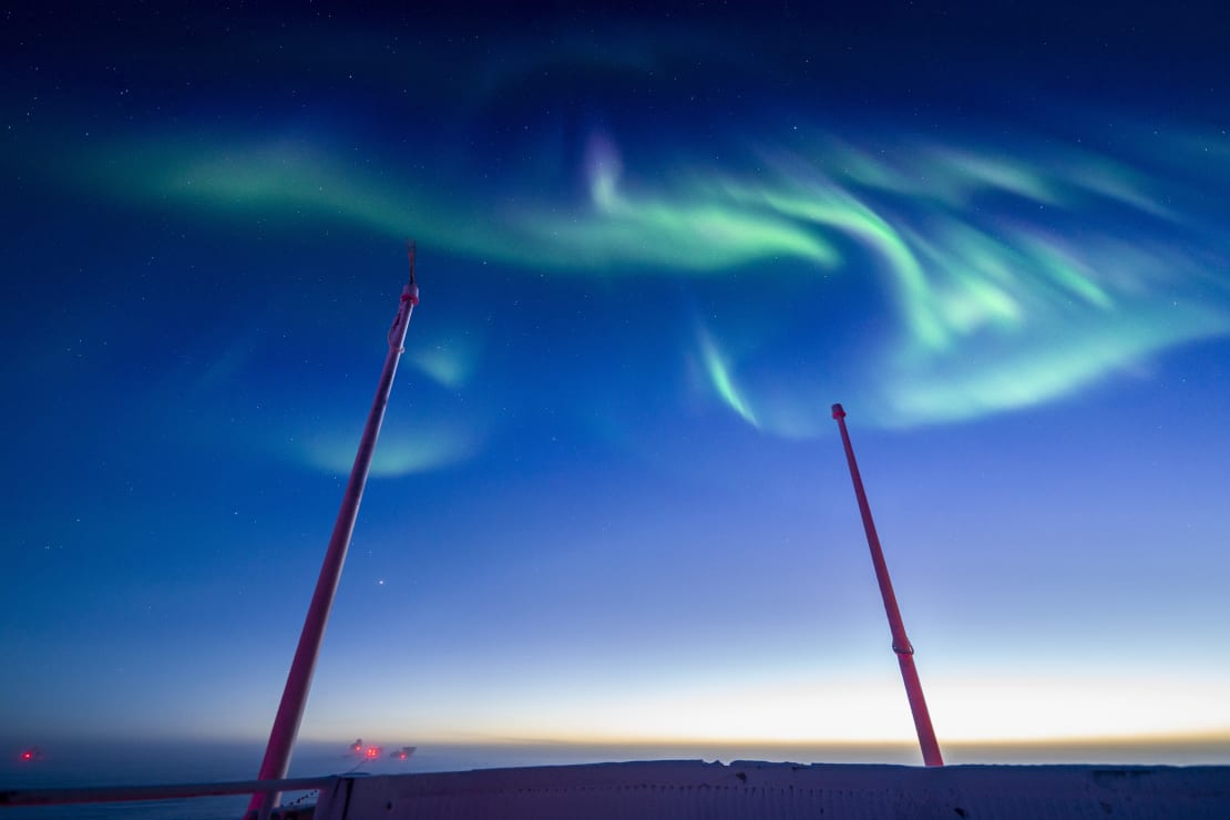 Swirling green auroras against blue sky, from observation deck of South Pole station.