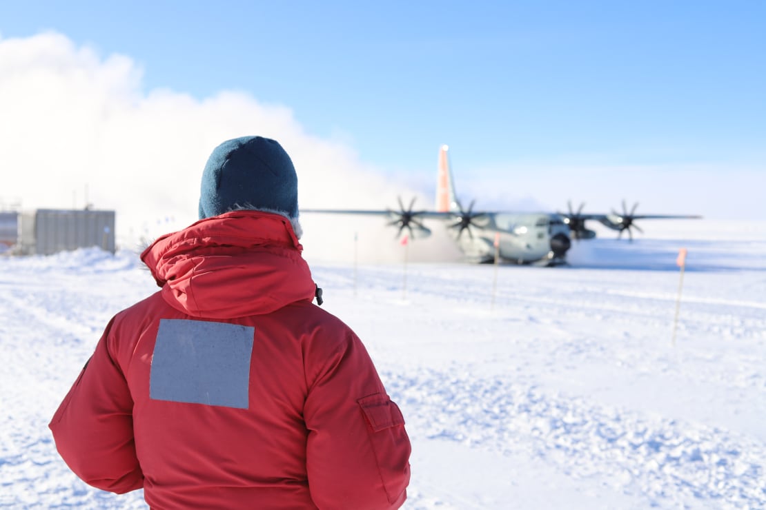 Backside of winterover watching an LC-130 on the South Pole skiway.