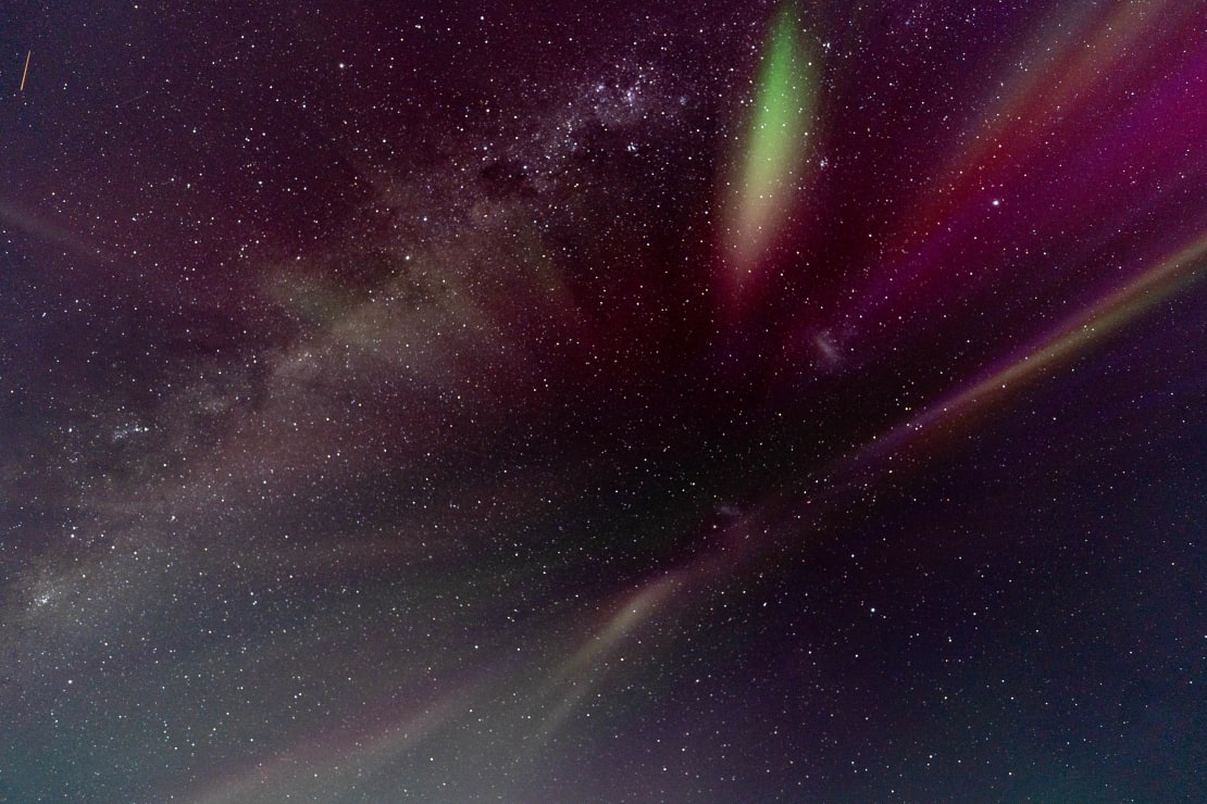 Looking upward into dark starry sky with lines of auroras fanning outward from center view.