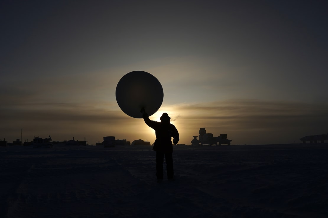 Shadow view of person standing and blocking sun behind them, holding a large weather balloon overhead.