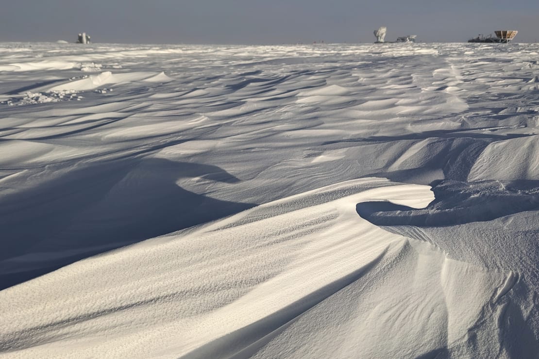 Sharp edges of sastrugi in early light from sunrise at the South Pole, Dark Sector buildings in far background.