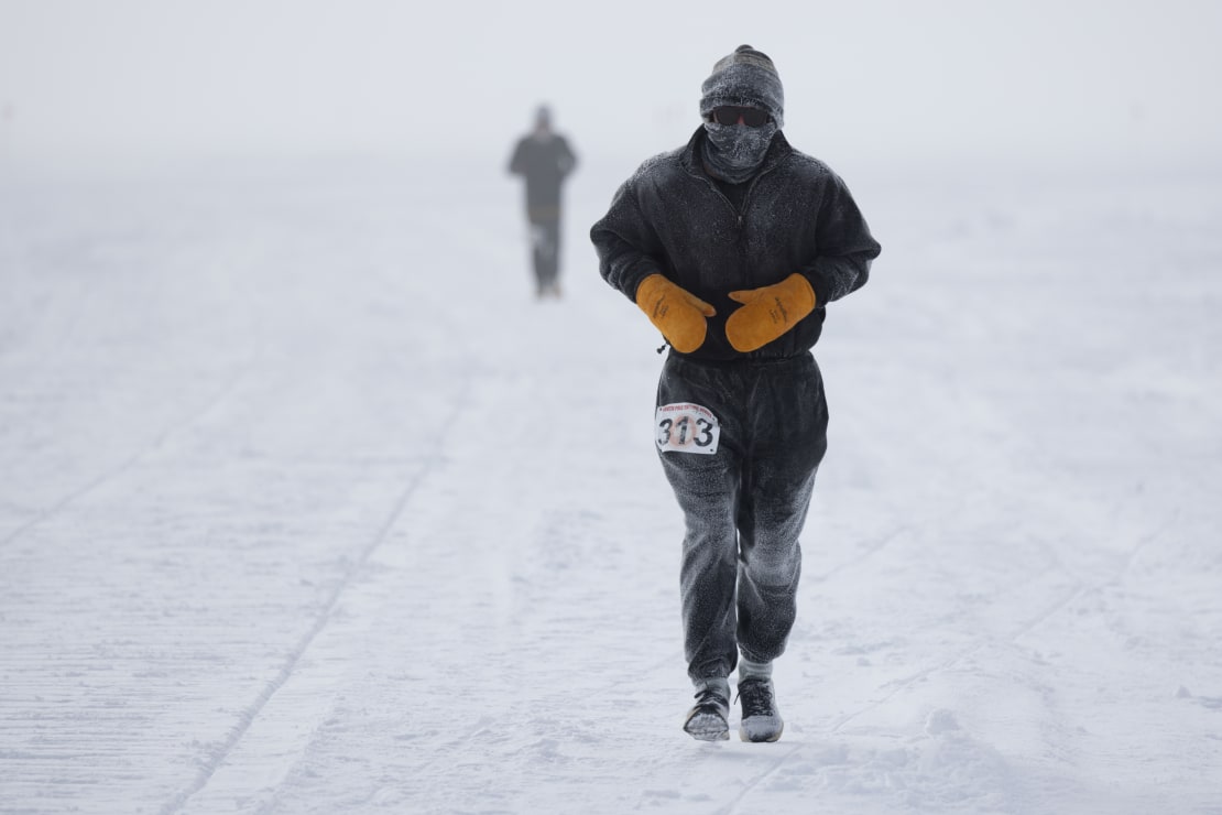 Person in dark outerwear seen head on as they run full marathon outside at the South Pole, with another person out of focus behind them.