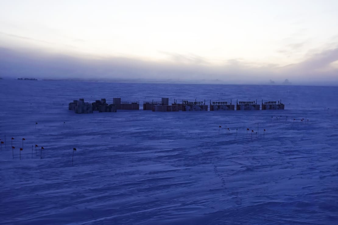 A string of equipment containers seen in dark shadow at the South Pole at sunset.
