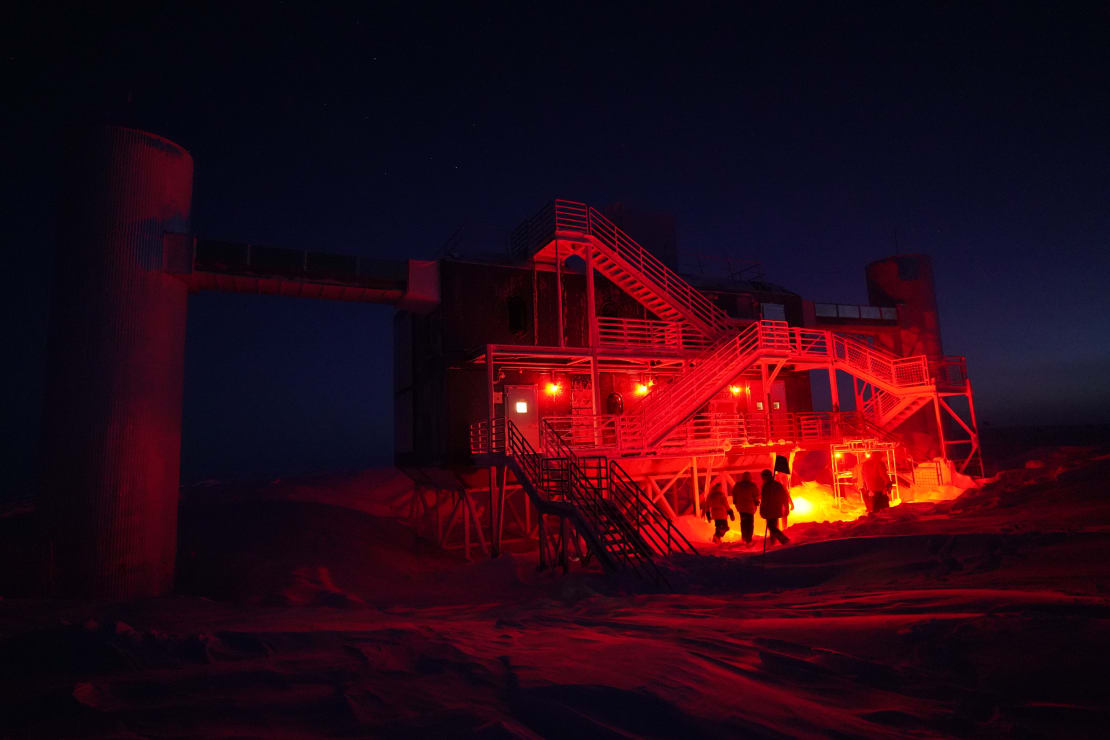 The IceCube Lab lit up in red while workers move about in darkness.