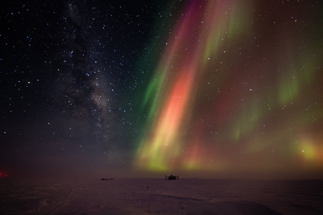 Colorful blaze of auroras filling the sky above the IceCube Lab on the distant horizon.