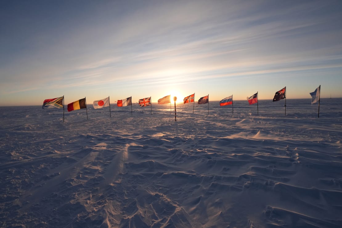 Low sun on the horizon behind the line of flags at the ceremonial South Pole.