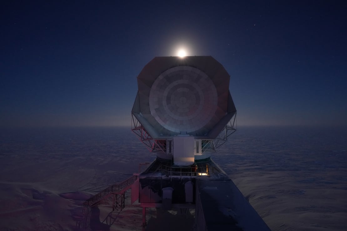 Bright moon centered over and peaking above the South Pole Telescope.