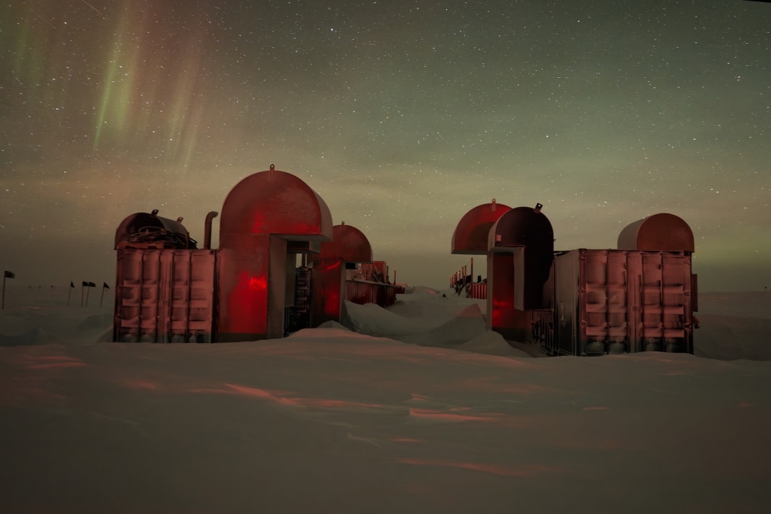 The IceCube drill camp structures sitting idle, softly lit by auroras.