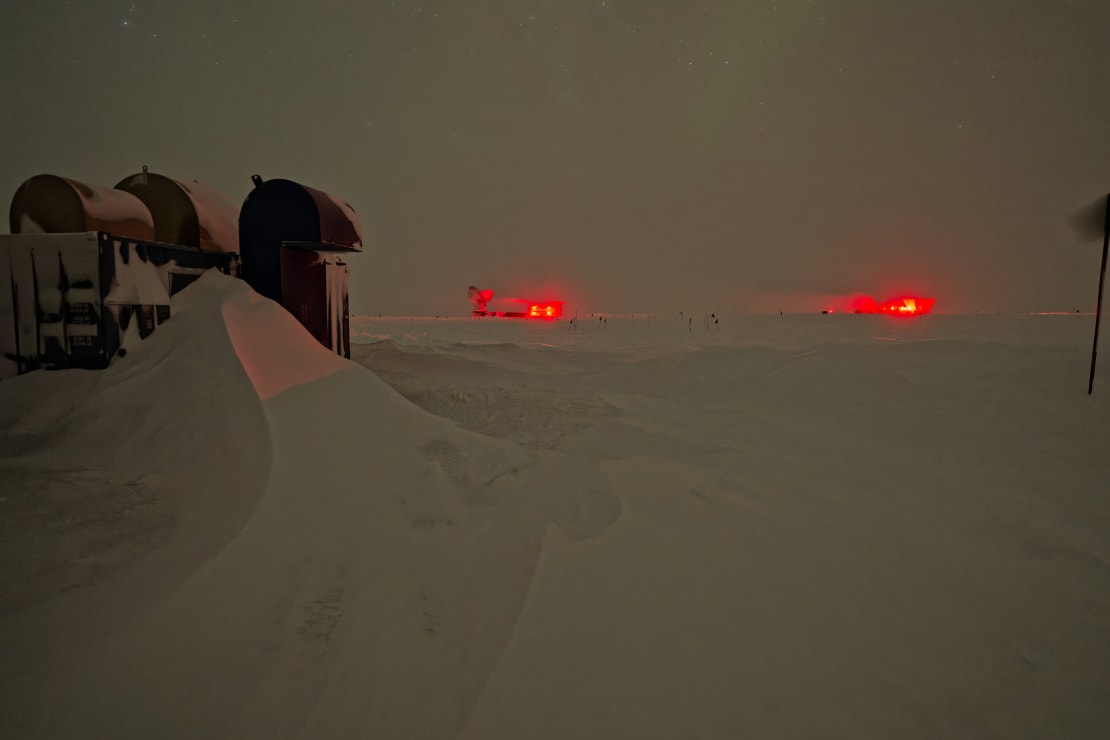 Snowdrift in foreground left, indirectly lit, two bright red lights on the horizon.