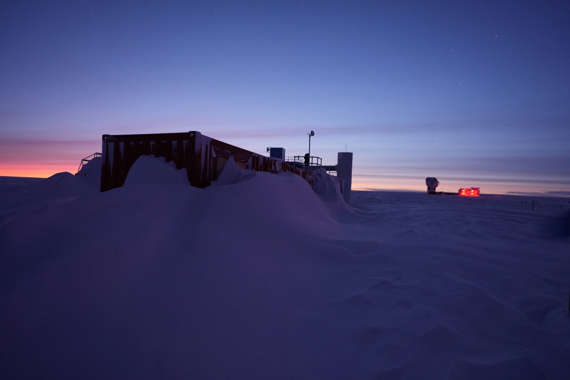 Storage building in shadow, with snow drifts up the sides, at South Pole twilight.