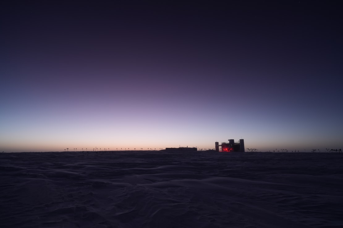 Dark blue sky with just faing light along horizon, IceCube Lab in shadow in distance.