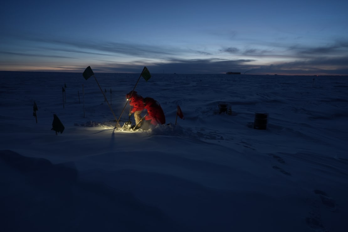 Winterover working outside, crouched with headlamp illuminating the ground.