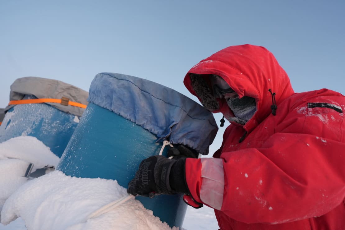 Closeup of person in red parka securing a cover on the top of a telescope apparatus.