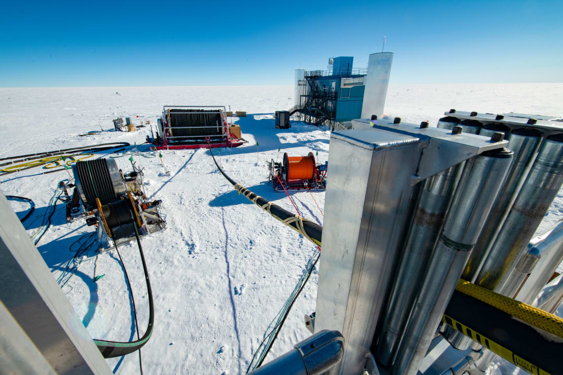 The drill tower with the drill hose and main cable running through with the IceCube Lab in the background.
