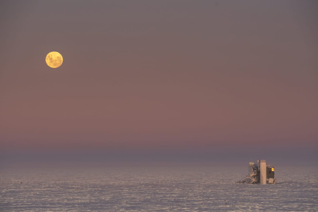 Full moon low in sky above IceCube Lab at sunrise.
