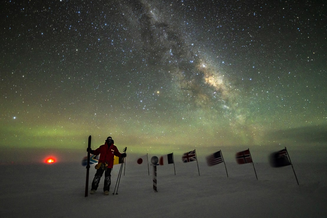 Winteover standing with ski poles at the ceremonial Pole with Milky Way overhead.