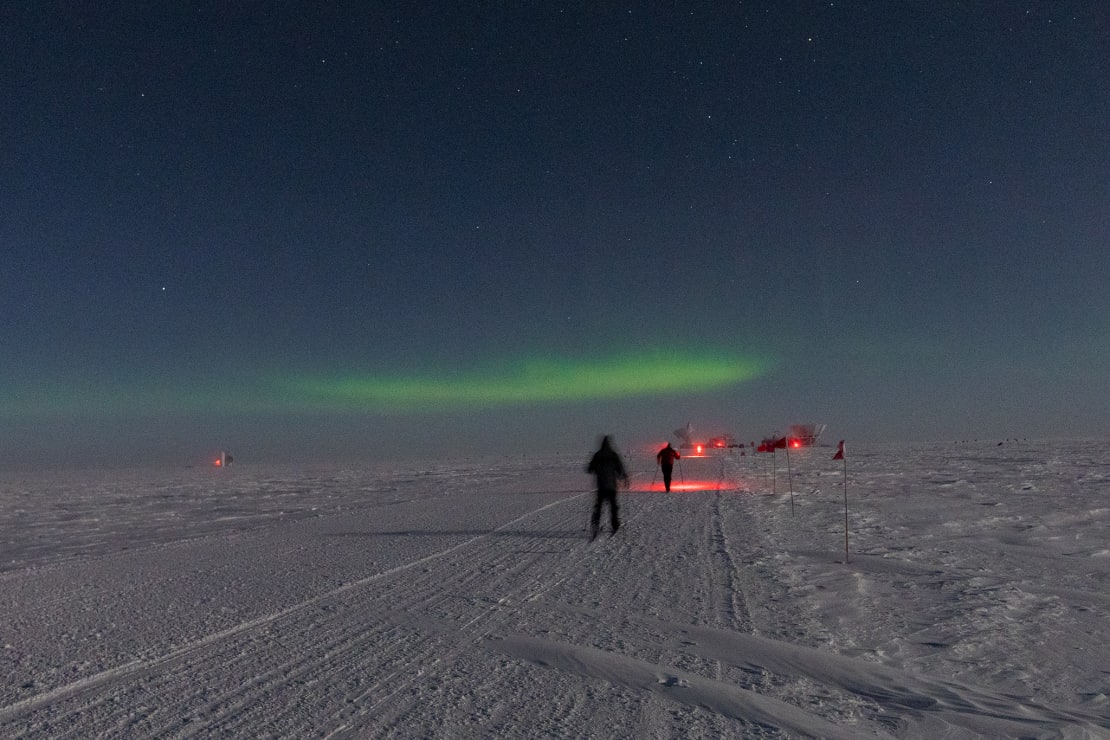 A couple of people skiing along a path at the South Pole under a starry sky.