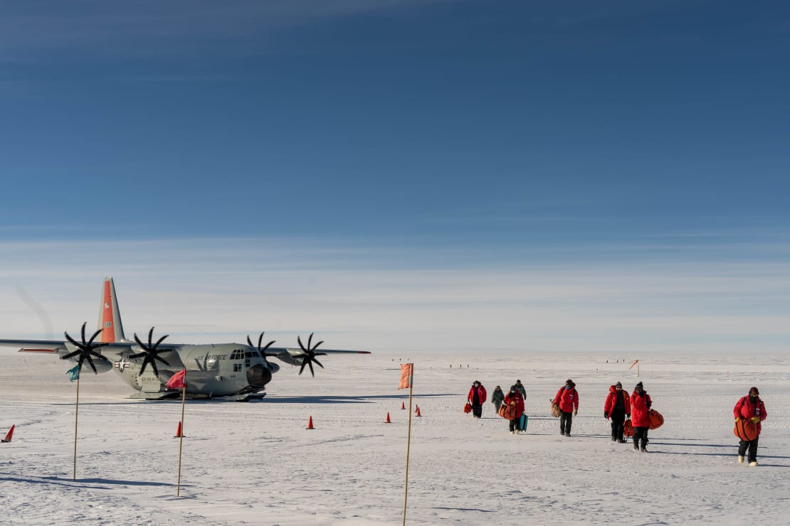 Group in red parkas walking away from plane parked on the skiway.
