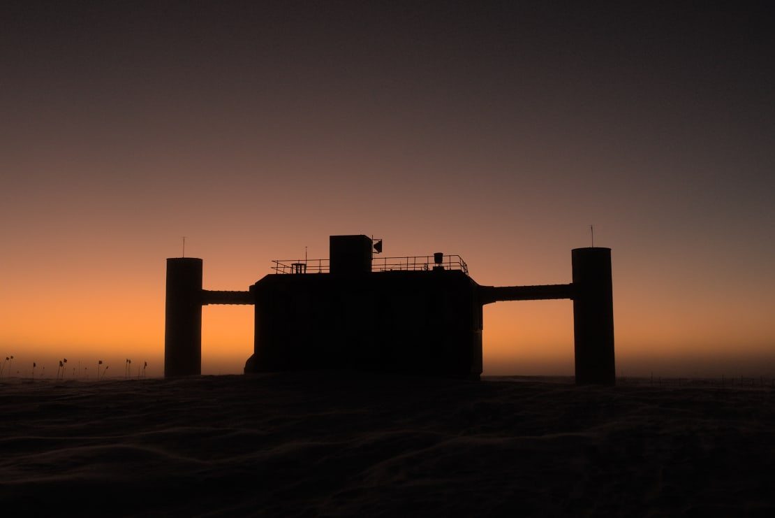 The IceCube Lab seen in shadow, with a bright orange sky along the horizon in background.