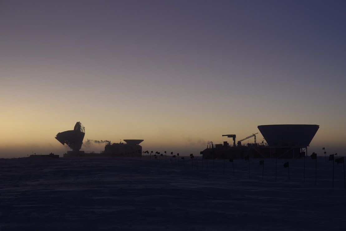 Dark sector buildings in shadow against pale light from early sunrise on the horizon.