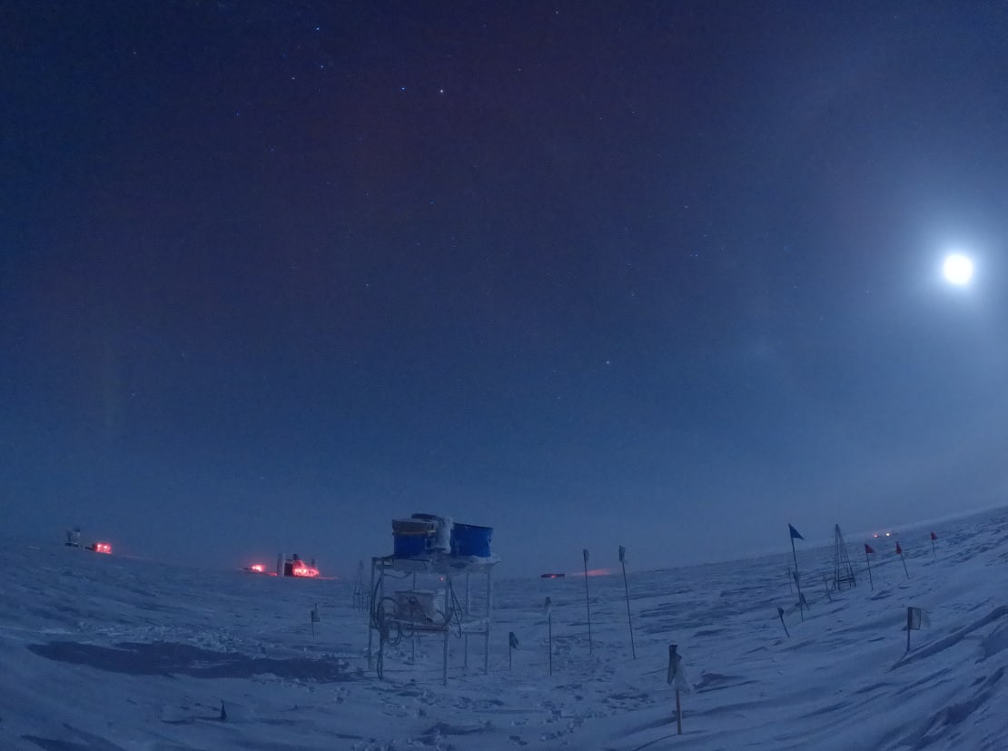 Bright moon over the site of the IceAct telescopes out on the ice, station visible on distant horizon.