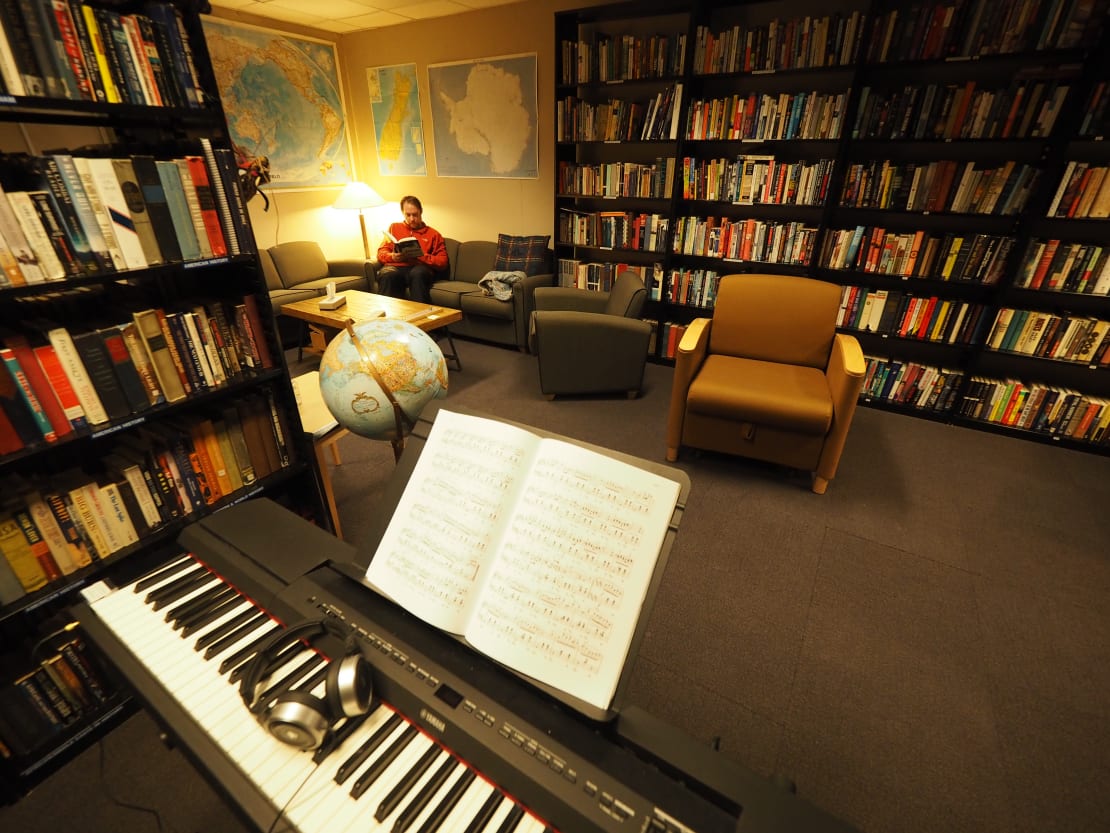 Person relaxing with a book on a sofa amid walls of bookshelves.