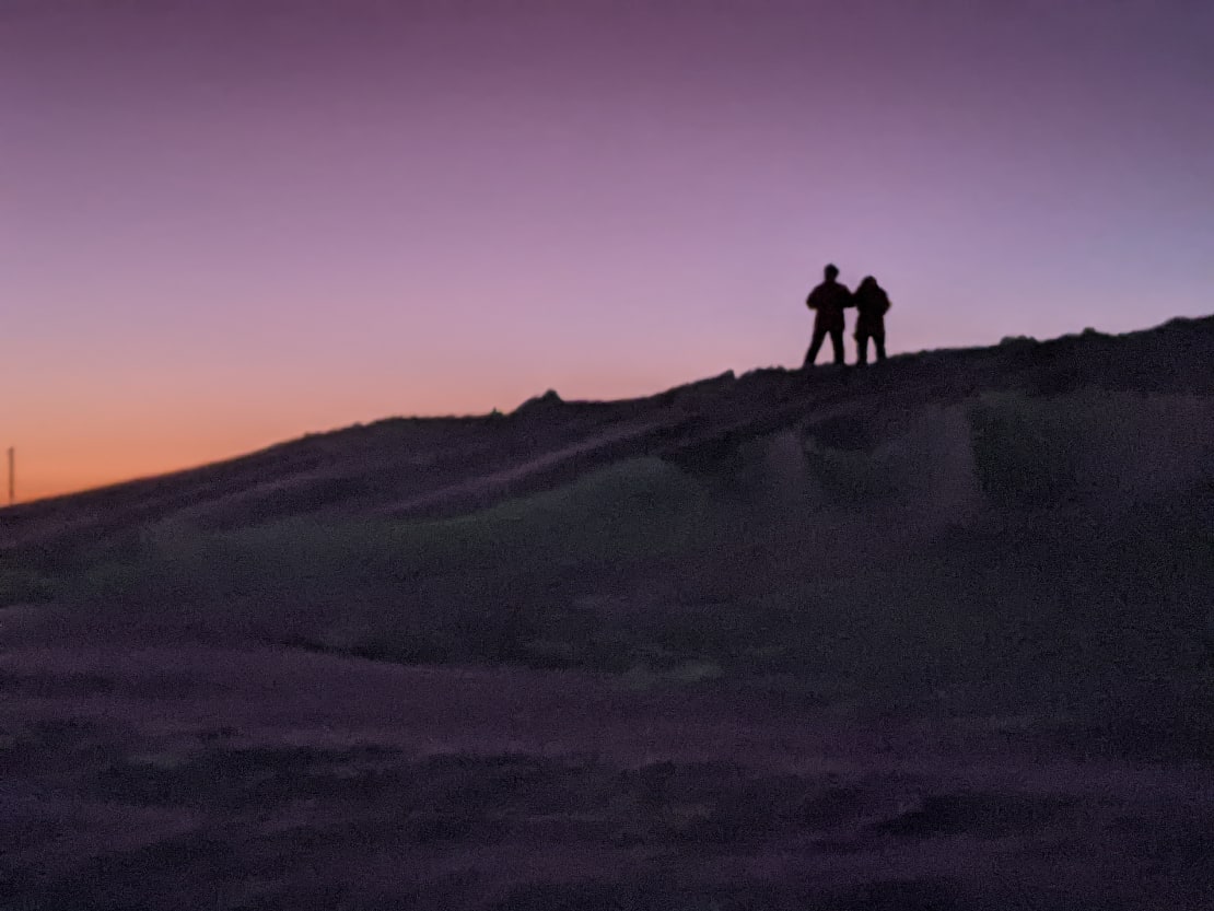 Two distant figures in shadow along ice ridge, purplish sky as background.