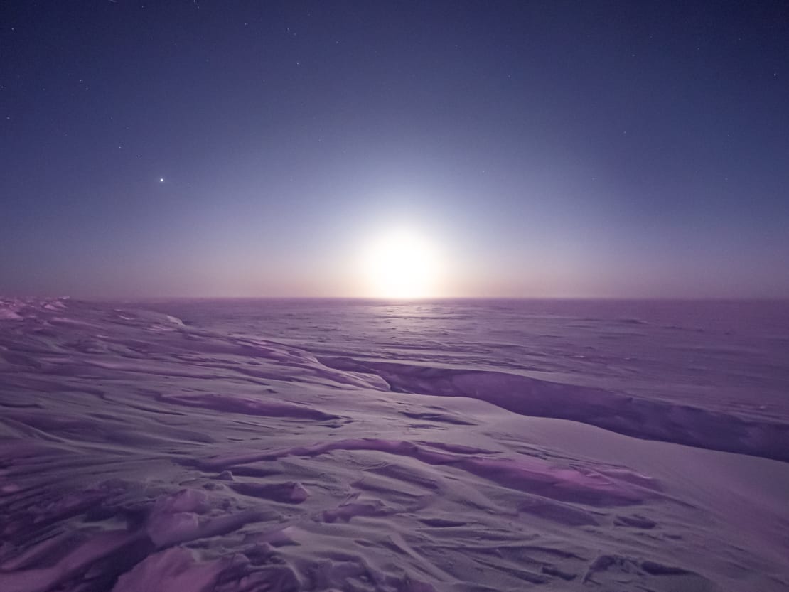 Icy barren landscape at South Pole with bright moon on horizon