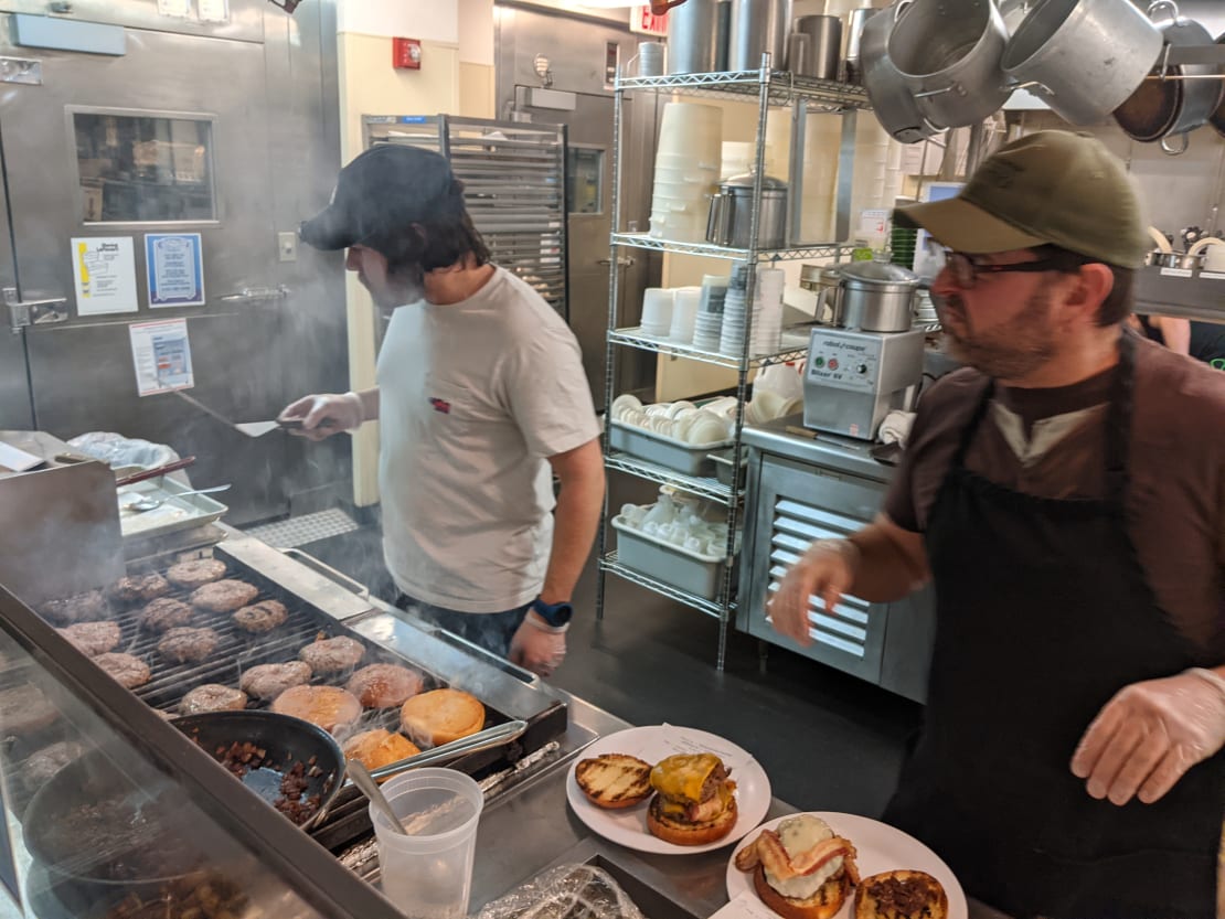 Two people grilling hamburgers in a kitchen.