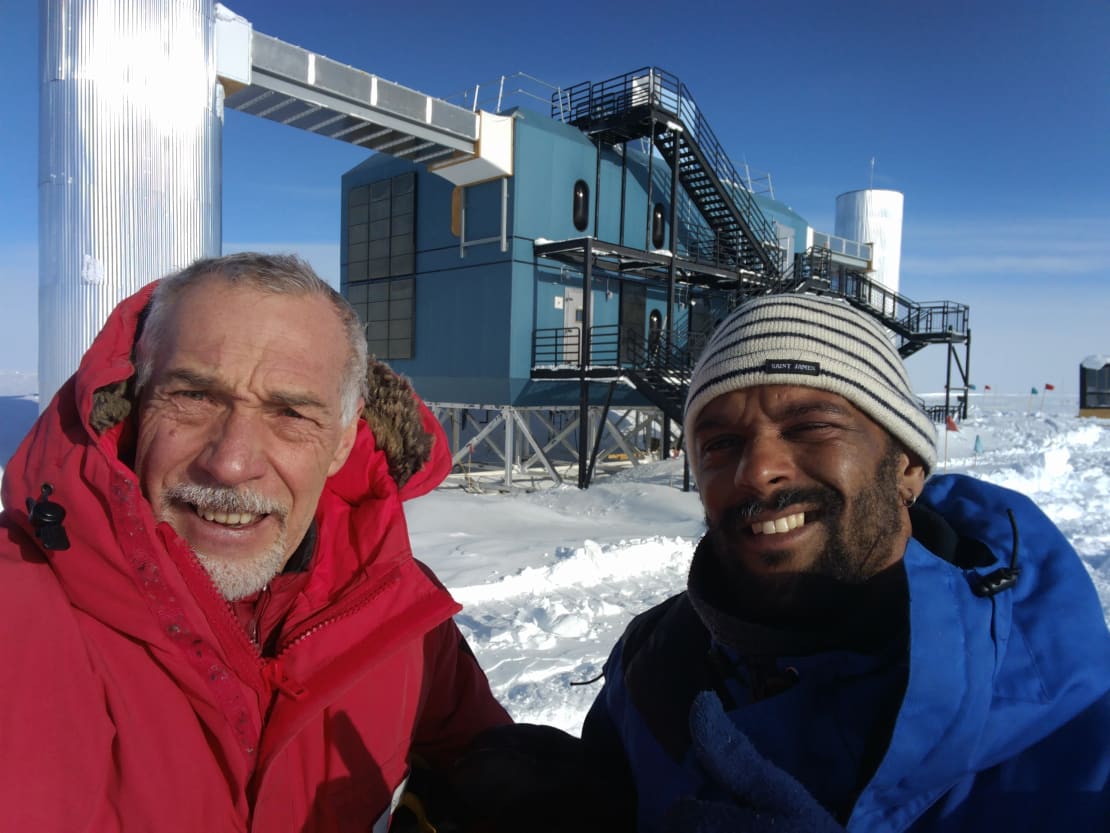 Two people close up in foreground, with IceCube Lab behind them.