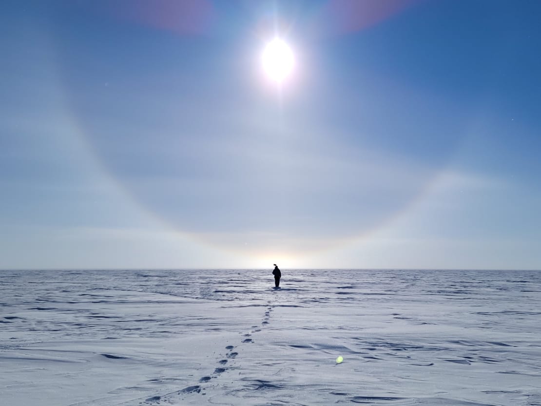 Person walking in distance under bright sun with sun halo.