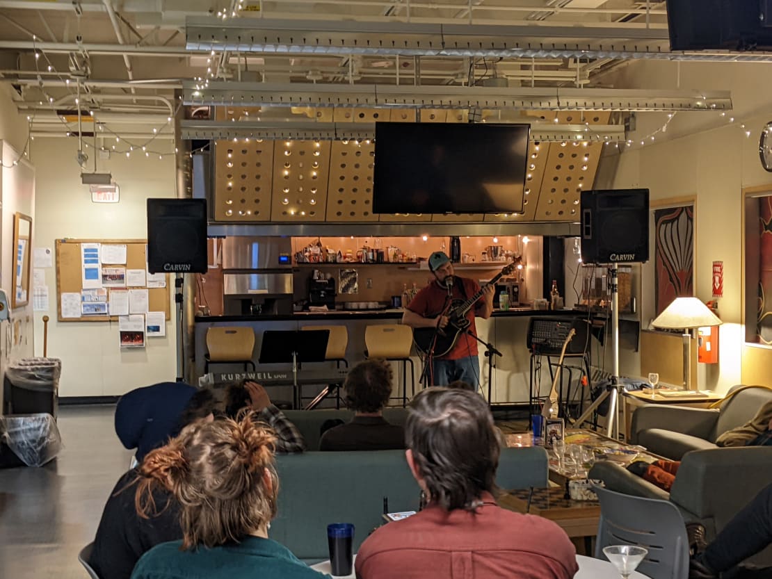 Person standing and playing the guitar for audience in the galley of the South Pole station.