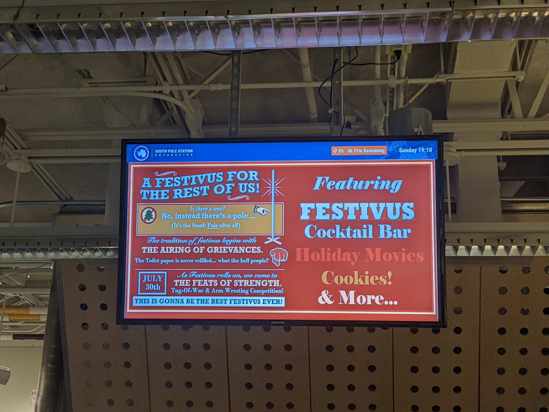 Monitor hung in South Pole galley displaying poster for upcoming Festivus celebration.